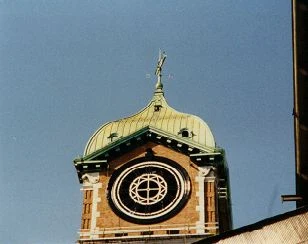 A clock tower with a green dome against a blue sky, its dial stripped to the iron frame during restoration.
